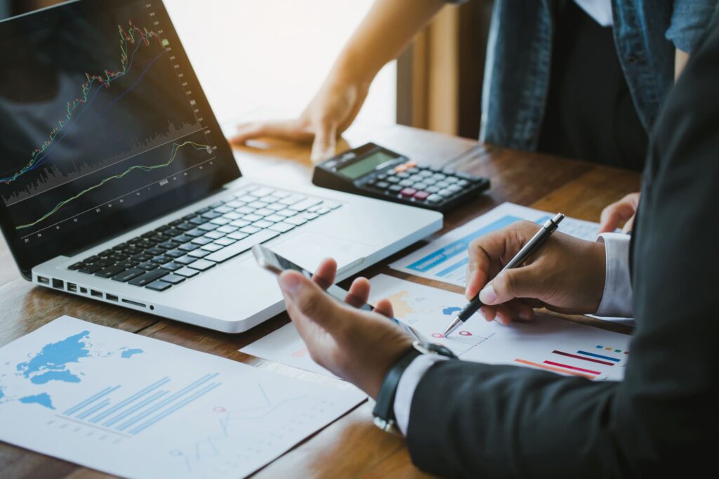 An image zoomed in to show a businessman holding a mobile phone and showing data charts on his computer screen.